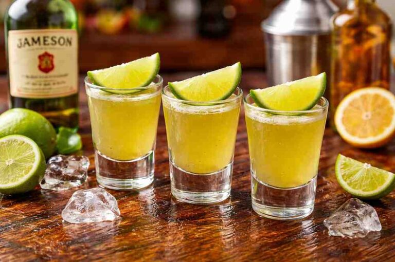 Green tea shot with lime wedges in shot glasses on wooden bar with whiskey and citrus ingredients